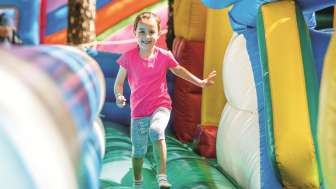 Une petite fille saute et court dans un château gonflable, le sourire aux lèvres.