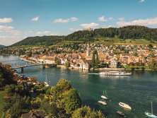 Vue de Stein am Rhein depuis l'autre rive du Rhin. Sur la colline, on voit le château de Hohenklingen et un bateau passe devant la vieille ville.
