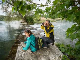 Deux randonneurs observent à la jumelle des animaux près de l'eau dans le parc naturel de Schaffhouse.