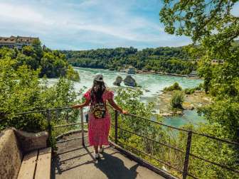 Une touriste porte une robe d'été et se tient à un point de vue pour contempler les chutes du Rhin.