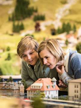 Une mère et son fils sont dans le monde miniature de Smilestones. Ils sont en train de regarder des maisons.