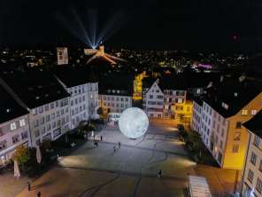Vue d'en haut, de nuit, sur le Munot illuminé. Des faisceaux de lumière brillent dans le ciel nocturne.