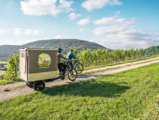Safari à vélo Schaffhauserland Deux amies se promènent dans les vignes avec leur vélo électrique. Sur un vélo-cargo, il y a une structure de tente dépliable.