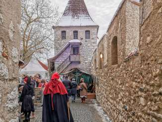 Marché médiéval Schloss Laufen am Rheinfall Une personne vêtue d'un habit médiéval et d'un bonnet rouge se promène dans la cour du château. Des stands de marché sont installés en bordure.