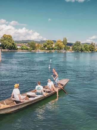 Promenade en weidling sur le Rhin Trois personnes et un chien sont assis dans le weidling. Le bateau en bois descend tranquillement le Rhin. Une femme est debout, elle tient une rame et dirige le bateau.