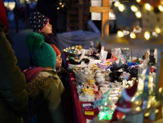 Marché de l'Avent à Neuhausen am Rheinfall Le soir, des enfants se tiennent devant un stand de marché et regardent des produits qu'ils ont fabriqués eux-mêmes. Le stand est décoré de lumières de Noël.