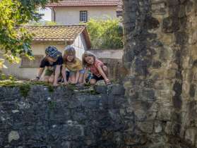 Trois enfants sont accroupis sur un mur de pierre dans un village.