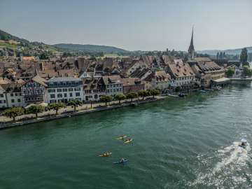 Trois canoës jaunes et un bleu naviguent sur le Rhin devant la vieille ville Stein am Rhein.
