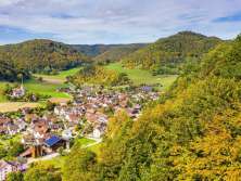 Vue depuis la forêt sur un village entouré de collines automnales couvertes de forêts. Une église se trouve légèrement à l'extérieur du village.