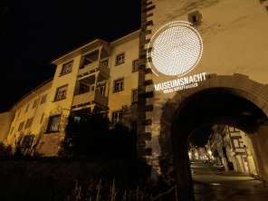 Nuit des musées Hegau-Schaffhouse Une ancienne façade de la ville avec un arc de porte dans la nuit. La façade est illuminée avec le slogan "Museumsnacht Hegau-Schaffhausen.