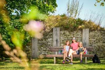 Une mère est assise sur un banc en bois avec ses deux filles.