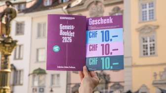 Eine Person hält das Genuss-Booklet in die Luft. Eine Broschüre mit Genusstipps und Gutscheinen zum Einlösen.