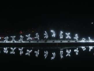 Lichtinstallation einer Person, die einen Sprung macht. Die Umrisse leuchten und spiegeln sich im Rhein.